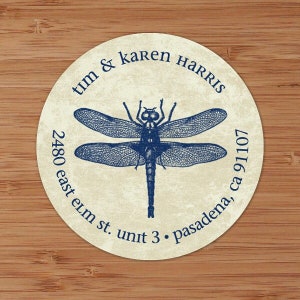 May include: A round, cream-colored sticker with a blue dragonfly illustration and the text "tim & karen HARRIS 2480 east elm st. unit 3. Pasadena, ca 91107"