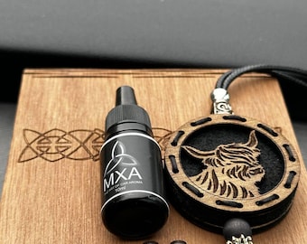 May include: A wooden box with a carved Celtic knot design holds a black bottle labeled "MXA Art of Car Aroma 10ml" and two small wooden pieces. A wooden pendant with a Highland cow design hangs nearby.