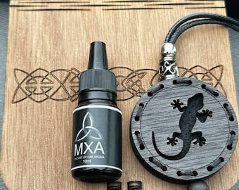May include: A wooden box with a Celtic knot design holds a black bottle labeled "MXA THE ART OF CAR AROMA 10ml" and a circular pendant with a lizard cutout. The pendant hangs from a black cord.