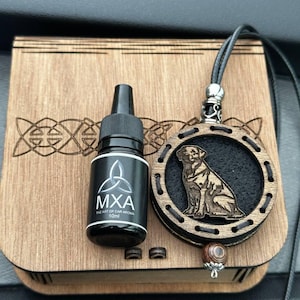 May include: A wooden box with Celtic knotwork, a black bottle labelled "MXA The Art of Car Aroma 10ml", and a wooden pendant with a dog carving. The pendant hangs from a black cord and has a decorative bead.