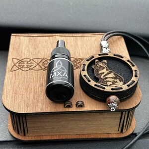 以下が含まれることがあります： ケルトノットのデザインの木箱、"MXA"とラベルされた小さな黒いボトル、彫刻された動物のデザインの木製ペンダント。ペンダントは黒いコードから吊り下げられ、装飾的なビーズが付いています。