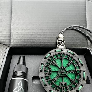 Puede incluir: Un juego de ambientador para coche negro. Incluye un colgante de madera con centro verde y símbolos rúnicos, y un frasco de 10 ml de aroma para coche. El colgante es redondo con un cordón negro.