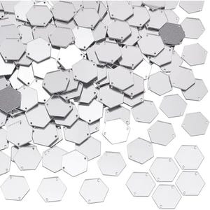 May include: A pile of shiny, silver hexagonal sequins. Each sequin has a reflective surface and small holes for sewing. The sequins are scattered, creating a textured, shimmering effect. Suitable for embellishing clothing or craft projects.
