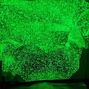 May include: A close-up of a glowing green fabric with a speckled pattern. The fabric appears layered and textured, with a bright, almost neon, green colour. The speckled pattern adds visual interest to the material.