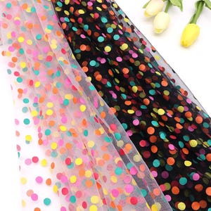 Puede incluir: Dos piezas de tela de tul transparente con un vibrante patrón de lunares. Una pieza es blanca y la otra es negra, ambas decoradas con puntos circulares multicolores en tonos rosa, naranja, amarillo y turquesa por todo el material.