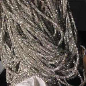 May include: Close-up of a pile of shimmering silver rhinestone strands. The strands are tightly woven together, creating a textured, sparkling effect. The rhinestones catch the light, creating a dazzling display. This item is perfect for jewelry making or embellishments.