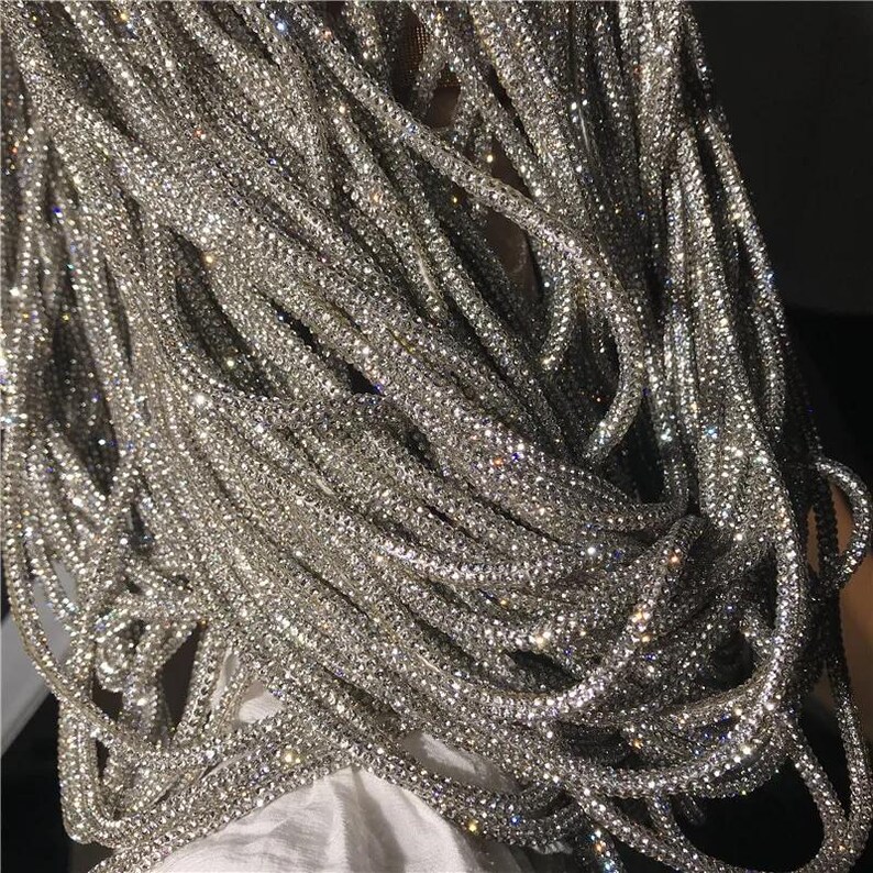 May include: Close-up of a pile of shimmering silver rhinestone strands. The strands are tightly woven together, creating a textured, sparkling effect. The rhinestones catch the light, creating a dazzling display. This item is perfect for jewelry making or embellishments.