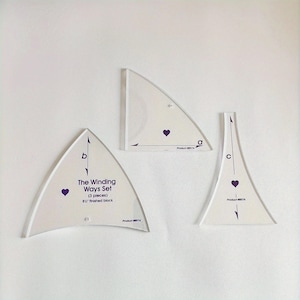 Pode incluir: Um conjunto de três modelos de acolchoado em acrílico transparente. Os modelos têm várias formas, incluindo um triângulo e uma forma curva. Cada modelo tem um coração roxo e marcações de medição. O texto "The Winding Ways Set" é visível.