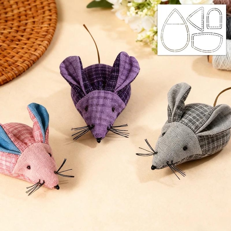 May include: Three handmade fabric mice in pink, purple, and grey plaid patterns. Each mouse has black whiskers, small black bead eyes, and a long, thin tail. The ears are a contrasting colour. A pattern template is in the background.