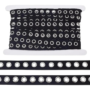 Può includere: Una bobina di nastro di tessuto nero con occhielli argentati distanziati uniformemente. Il nastro è avvolto strettamente, con diverse file visibili. Sotto sono mostrate due strisce aggiuntive del nastro.