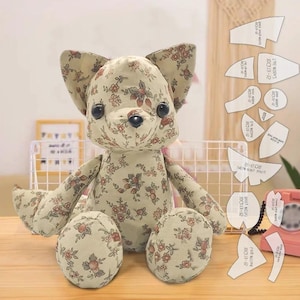 Puede incluir: Un juguete de peluche de perro de tela floral hecho a mano con orejas grandes, ojos de botón negros y una nariz negra. El perro está sentado sobre una superficie de madera. Se ven patrones de costura en el fondo.