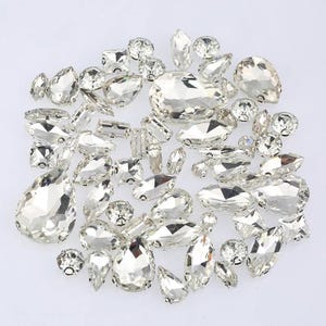 May include: A collection of clear, faceted rhinestones in various shapes and sizes, including teardrops, ovals, and rounds. These sparkling embellishments are ideal for crafting, jewelry making, or adding a touch of glamour to any project.