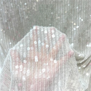 May include: A sheer white mesh fabric featuring vertical rows of small, square, iridescent sequins. The lightweight, semi-transparent material has a fine grid-like texture, with the reflective sequins spaced evenly along the vertical lines.