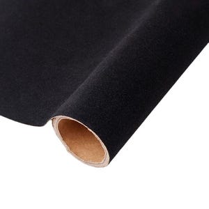 Op de afbeelding: Een rol zwarte fluwelen stof. De stof is strak opgerold en onthult een bruine kartonnen kern. Het fluweel heeft een zacht, getextureerd uiterlijk en de kleur is een diep, effen zwart.