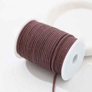 May include: A spool of mauve-colored rhinestone trim. The trim is tightly wound on a white plastic spool. The rhinestones are small and closely set, creating a continuous, sparkling surface. The trim is suitable for various craft and design projects.