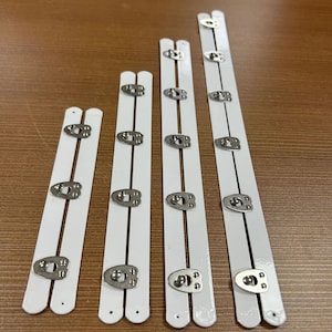 Puede incluir: Varios soportes de rieles de cama de metal blanco con herrajes plateados. Los soportes son de diferentes longitudes y tienen múltiples puntos de conexión. Los herrajes parecen estar remachados al metal blanco.