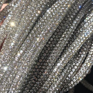 May include: Close-up of multiple strands of sparkling, silver rhinestones. The rhinestones are densely packed, creating a shimmering, reflective surface. The strands are slightly curved, and the overall effect is one of luxury and glamour.