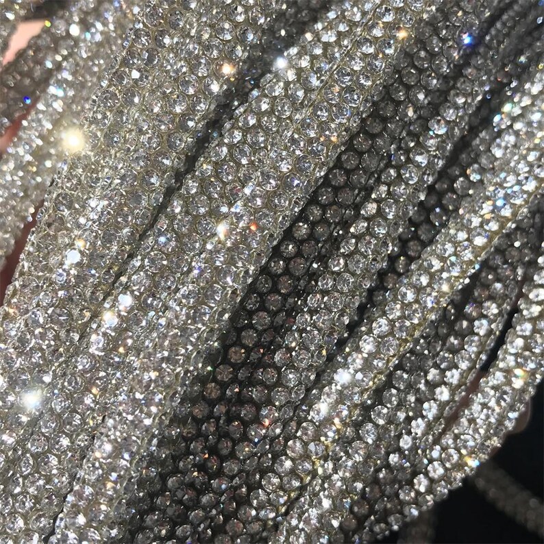 May include: Close-up of multiple strands of sparkling, silver rhinestones. The rhinestones are densely packed, creating a shimmering, reflective surface. The strands are slightly curved, and the overall effect is one of luxury and glamour.