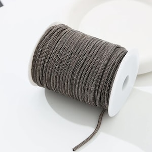May include: A spool of brown braided cord. The cord is tightly wound around a white plastic spool. The cord has a slightly metallic sheen, and a small length of the cord extends from the spool.