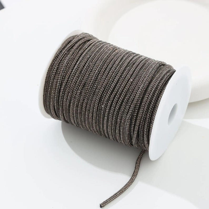 May include: A spool of brown braided cord. The cord is tightly wound around a white plastic spool. The cord has a slightly metallic sheen, and a small length of the cord extends from the spool.