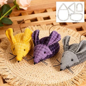 May include: Three fabric toy mice in yellow, purple, and grey, each with black whiskers and a brown string tail. The mice are arranged on a woven mat, suggesting a playful theme.