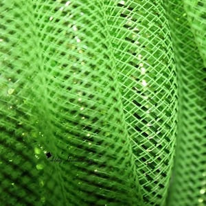 May include: Close-up of vibrant green mesh fabric with a diamond pattern. The fabric has a shiny, glittery texture, with small, reflective particles scattered throughout. The mesh is tightly woven, creating a textured surface.