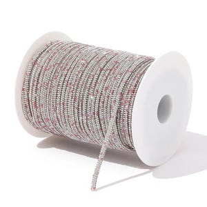 May include: A spool of silver rhinestone chain with small pink accents. The chain is tightly wound on a white plastic spool. The rhinestones are small and closely set, creating a sparkling effect. Ideal for jewelry making and crafts.