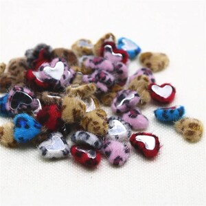 May include: A collection of small, heart-shaped embellishments with a furry texture. The hearts feature a variety of colors, including brown, pink, red, and blue, with a silver heart-shaped accent in the center. Some have a leopard print pattern.