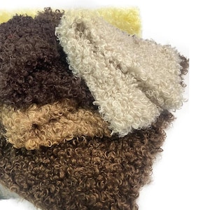 Può includere: Una collezione di pelli di pecora ricce e strutturate in vari colori naturali. I colori vanno dal marrone scuro al crema e al beige, con una tonalità gialla sullo sfondo. Le pelli sono disposte in una composizione a strati.