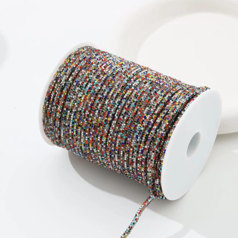 May include: A spool of colorful, beaded trim. The trim is tightly wound on a white plastic spool. The beads are a mix of colors, including red, blue, green, and gold. The trim is likely used for crafting or embellishment.