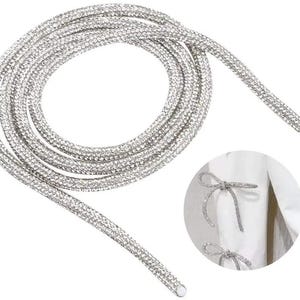 May include: Silver rhinestone shoelaces coiled on a white background. The shoelaces are covered in small, sparkling rhinestones. A close-up shows the shoelaces tied into a bow on a white garment.