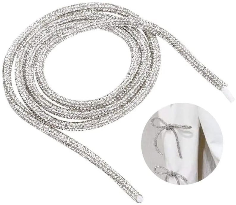 May include: Silver rhinestone shoelaces coiled on a white background. The shoelaces are covered in small, sparkling rhinestones. A close-up shows the shoelaces tied into a bow on a white garment.
