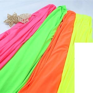 Könnte beinhalten: Leuchtende Stoffe in Pink, Grün, Orange und Gelb. Der Stoff ist drapiert und gefaltet, wodurch ein fließender Effekt entsteht. Zwei gewebte sternförmige Dekorationen befinden sich in der oberen linken Ecke.