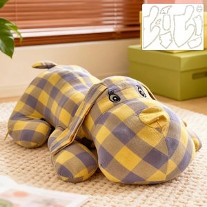 May include: A dog-shaped cushion in a yellow and grey check pattern. The soft toy has long, floppy ears, a stitched nose, and embroidered eyes. A pattern for the cushion is visible in the background.