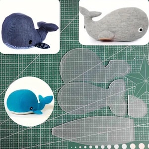 Op de afbeelding: Een verzameling walvis-thema items, waaronder drie pluche walvissen in blauw, grijs en denim, en transparante walvis patroonsjablonen. De walvissen hebben eenvoudige, afgeronde vormen, op een groene snijmat.