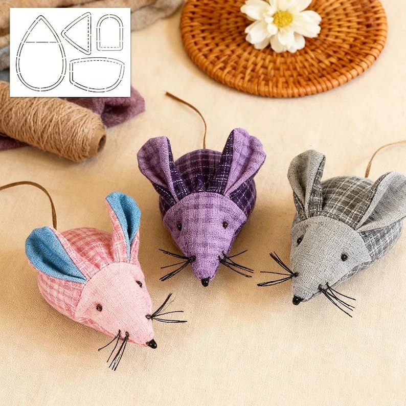 May include: Three fabric mouse toys in pink, purple, and grey plaid patterns. Each mouse has long ears, black whiskers, and a brown string for hanging. A pattern for the mouse is visible in the upper left corner.