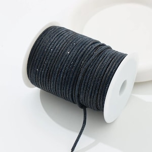 May include: A spool of dark blue, sparkly cord. The cord is tightly wound around a white plastic spool. The cord has a subtle sheen and is suitable for various crafting projects. The cord is a dark navy blue color.