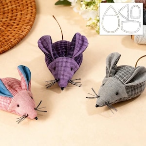 May include: Three fabric mice in pink, purple, and grey with plaid patterns. Each mouse has black whiskers, small black bead eyes, and a long, thin tail. The ears are a contrasting colour. A pattern template is in the background.