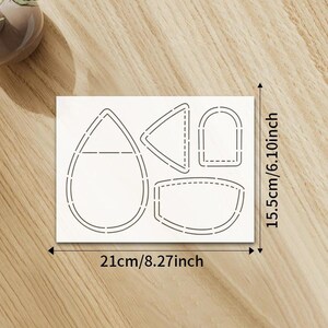 May include: A white paper featuring die-cut shapes, including a teardrop, triangle, and curved rectangles. The paper measures 21cm wide and 15.5cm high. The shapes are outlined with dashed lines, suitable for crafting or design projects.