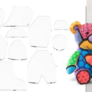 Può includere: Un orsacchiotto patchwork colorato con una varietà di motivi e colori, tra cui pois blu, strisce e un design a cuore. Sono presenti anche modelli di cucito in acrilico trasparente.