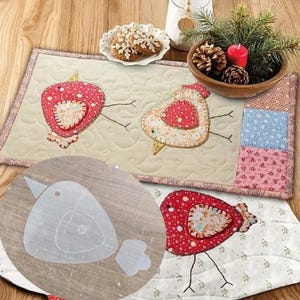 May include: A quilted table runner with two appliqued bird designs in red and cream fabrics. The birds are on a cream background with a floral border. A clear bird-shaped template is in the foreground. The runner is on a wooden surface.