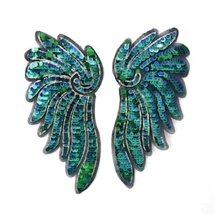 Può includere: Una coppia di toppe ricamate a forma di ala con paillettes iridescenti verdi e blu disposte in un motivo a piume stratificate. Ogni toppa presenta un bordo in tessuto grigio scuro e un design curvo che imita la forma di ali di uccello.