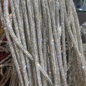 May include: Close-up of multiple strands of silver rhinestones, densely packed and hanging vertically. The strands are uniform in width and sparkle, reflecting light. The overall effect is glamorous and decorative.