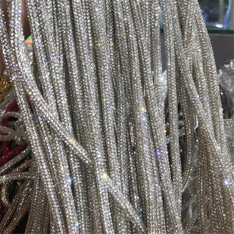 May include: Close-up of multiple strands of silver rhinestones, densely packed and hanging vertically. The strands are uniform in width and sparkle, reflecting light. The overall effect is glamorous and decorative.