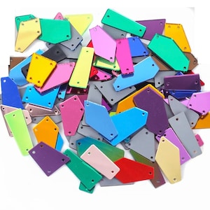 Puede incluir: Un conjunto de piezas geométricas de acrílico multicolor. Las piezas son de color rosa, azul, verde, amarillo y morado, con un acabado metálico reflectante. Cada pieza tiene dos pequeños agujeros.