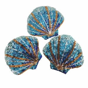 May include: Three sequined seashell appliques. The shells are a mix of blue and silver sequins, with gold-colored sequin stripes radiating from the center. The appliques are on a white background.
