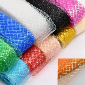 May include: A collection of rolls of glittery tulle ribbon in various colors including white, black, pink, blue, green, red, peach, and gold. Each roll features a diamond-shaped grid pattern with a shimmering, iridescent finish.