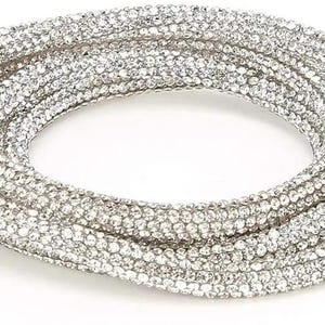 May include: A coiled, silver-colored necklace densely covered in small, sparkling rhinestones. The necklace is displayed against a white background, highlighting its reflective qualities and intricate design. The overall aesthetic is glamorous and eye-catching.