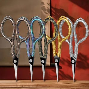 May include: A collection of six decorative scissors with ornate handles in various metallic finishes. The scissors have black blades and are arranged in a row, showcasing their intricate designs and colors.