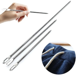 May include: Three long, slender, silver-colored metal needles with flat, elongated eyes at one end for threading. The needles are straight with pointed tips. A circular inset shows a close-up of a white drawstring threaded through blue fabric.